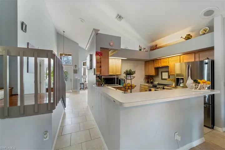 Kitchen with kitchen peninsula, light tile patterned floors, backsplash, and high vaulted ceiling