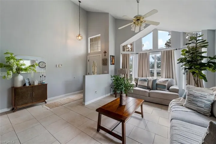Living room with high vaulted ceiling, light tile patterned floors, and ceiling fan