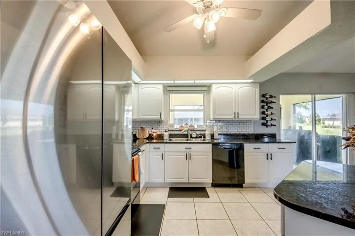 Kitchen with stainless steel appliances, dark stone counters, white cabinetry, light tile patterned floors, and decorative backsplash