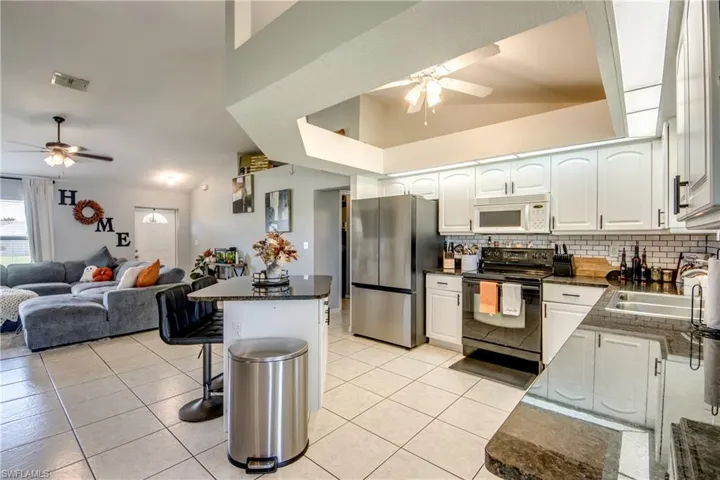 Kitchen featuring a ceiling fan, white cabinetry, black range with electric cooktop, freestanding refrigerator, and vaulted ceiling