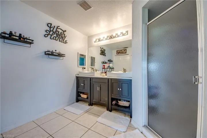 Full bathroom featuring double vanity, a stall shower, light tile patterned flooring, and a textured ceiling