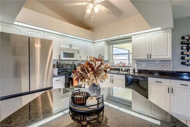 Kitchen featuring black appliances, dark stone counters, white cabinetry, tasteful backsplash, and a ceiling fan