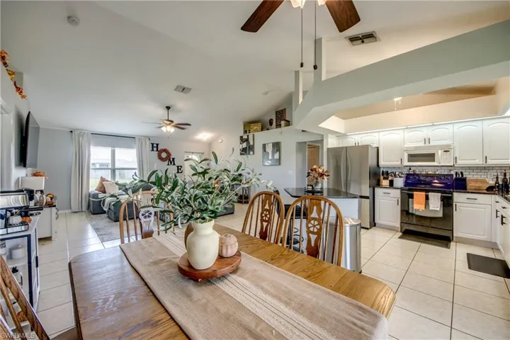 Dining room with ceiling fan, light tile patterned floors, and vaulted ceiling
