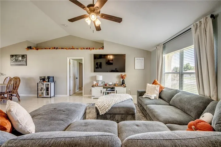 Living room featuring vaulted ceiling, ceiling fan, and light tile patterned floors