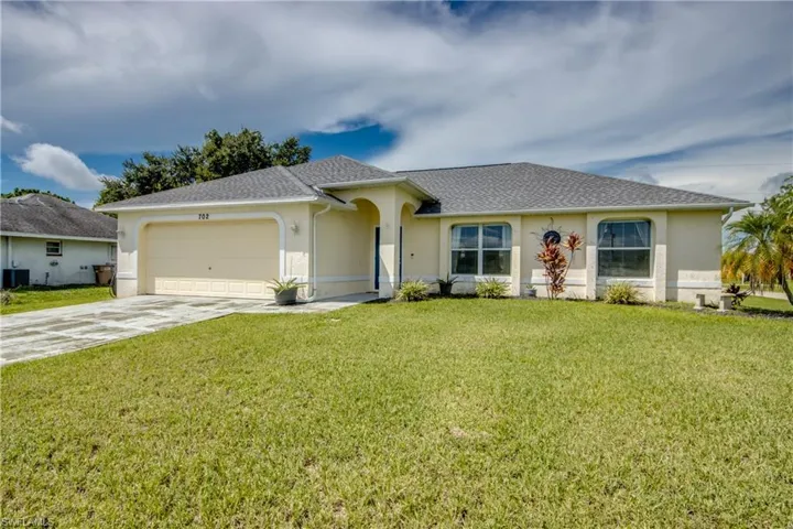 Ranch-style home featuring driveway, a front yard, stucco siding, an attached garage, and roof with shingles