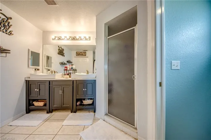 Full bath with double vanity, a stall shower, a textured wall, light tile patterned floors, and a textured ceiling