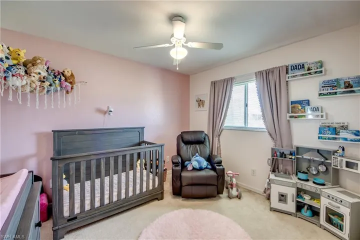 Bedroom featuring light carpet, a crib, and a ceiling fan