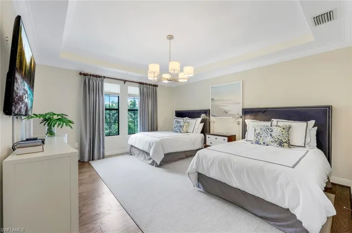 Bedroom with crown molding, a tray ceiling, a notable chandelier, and light hardwood / wood-style floors