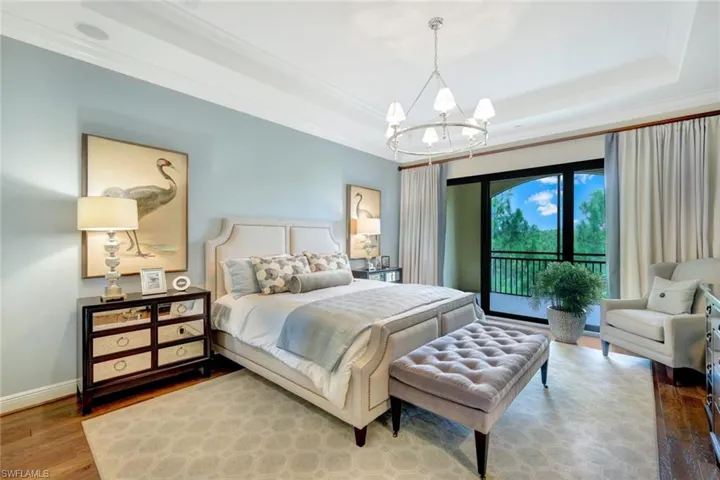 Bedroom featuring hardwood / wood-style flooring, a tray ceiling, ornamental molding, an inviting chandelier, and access to outside