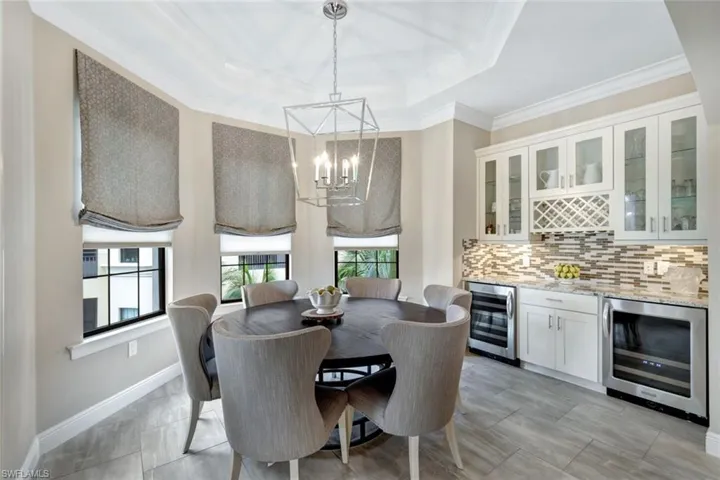 Dining space featuring light tile patterned flooring, a tray ceiling, a notable chandelier, wine cooler, and white cabinets