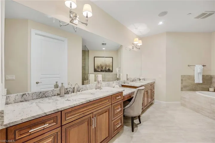 Bathroom with double vanity, tiled bath, a notable chandelier, and tile patterned floors
