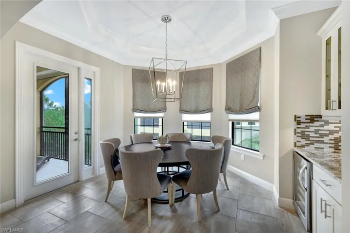 Tiled dining room featuring plenty of natural light, a tray ceiling, wine cooler, and a notable chandelier