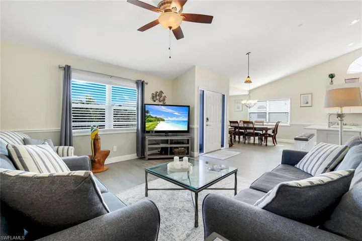 Living room featuring ceiling fan with notable chandelier, light wood-type flooring, vaulted ceiling, and a healthy amount of sunlight