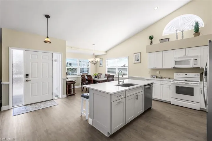 Kitchen with white appliances, decorative light fixtures, a kitchen island with sink, and sink