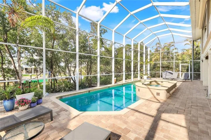 View of pool featuring glass enclosure, a patio area, and an in ground hot tub