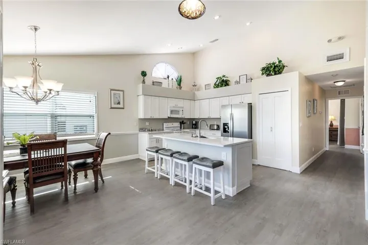Kitchen featuring a healthy amount of sunlight, white appliances, an island with sink, and white cabinetry