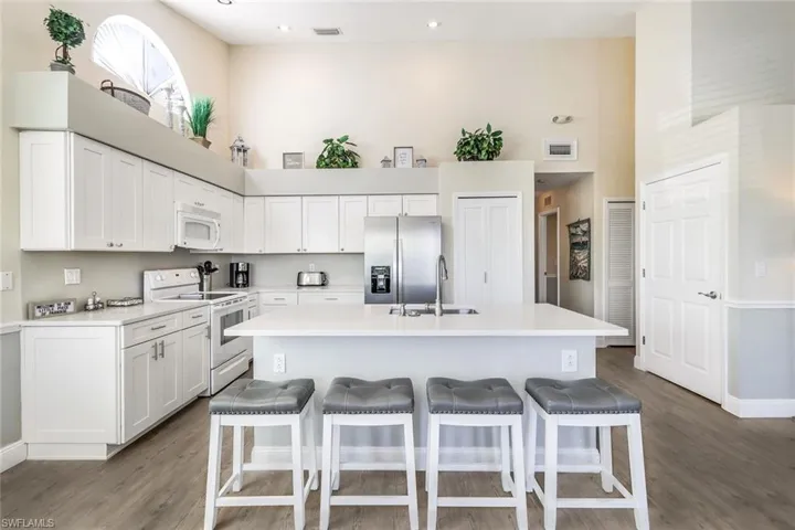 Kitchen featuring white cabinets, white appliances, a center island with sink, and sink