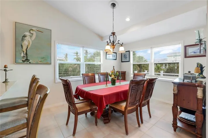 Tiled dining room with a healthy amount of sunlight, vaulted ceiling, and an inviting chandelier