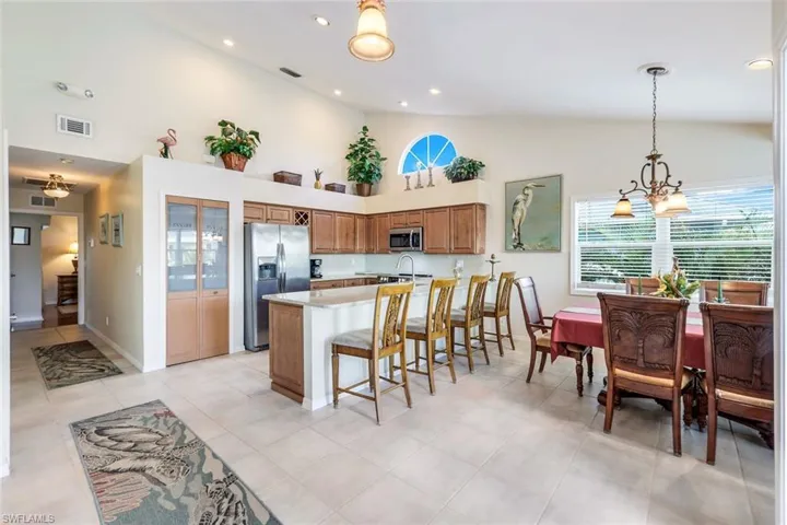 Kitchen with high vaulted ceiling, a chandelier, decorative light fixtures, a kitchen bar, and appliances with stainless steel finishes