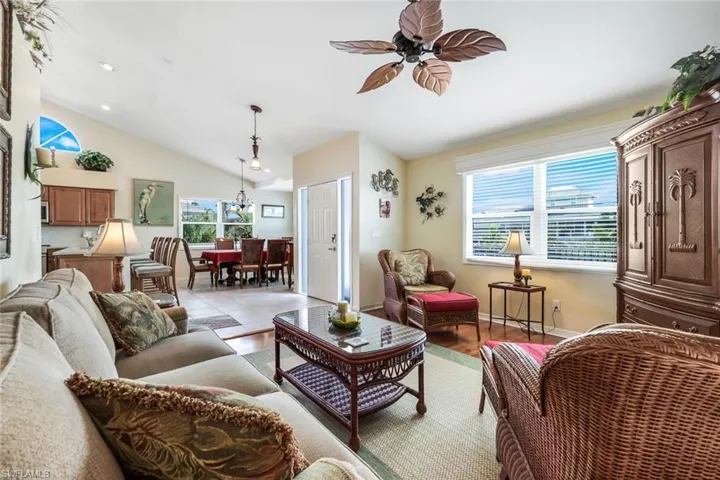 Living room with ceiling fan with notable chandelier, light wood-type flooring, and lofted ceiling