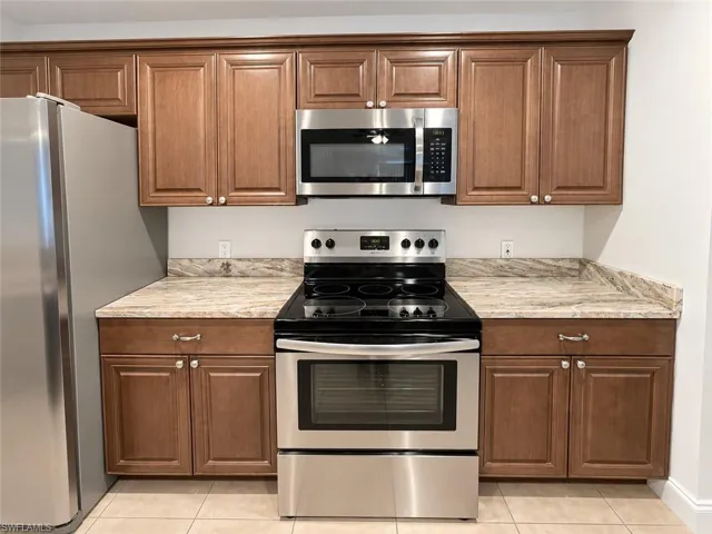 Kitchen featuring wood-finish cabinetry, stainless steel appliances, light-toned countertops, and tiled flooring