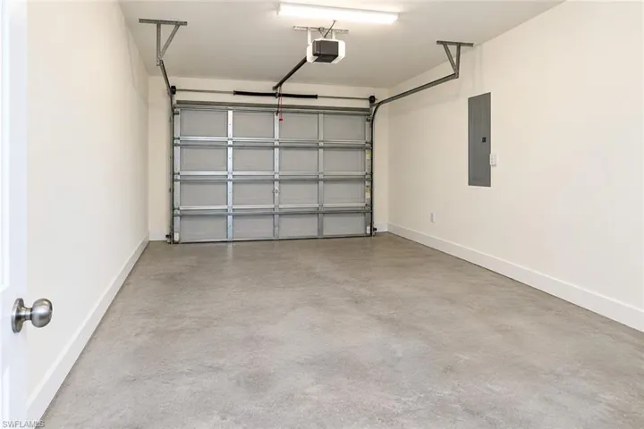 Concrete flooring, white painted walls, overhead garage door system, exposed electrical panel