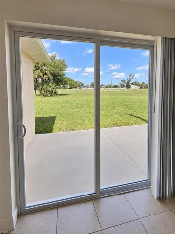 Sliding glass door opening to a concrete patio and expansive green space