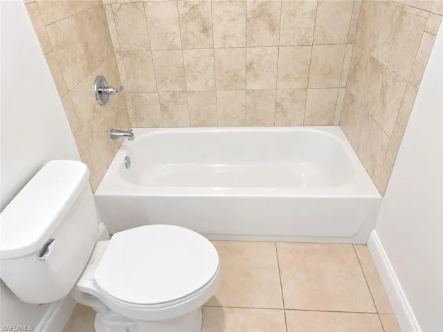 White bathtub with chrome fixtures, complemented by a tiled surround and coordinating floor tiles