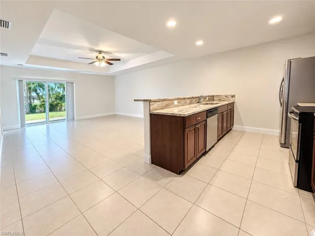 Open-concept living space featuring tiled flooring, a tray ceiling with a ceiling fan, and sliding glass doors