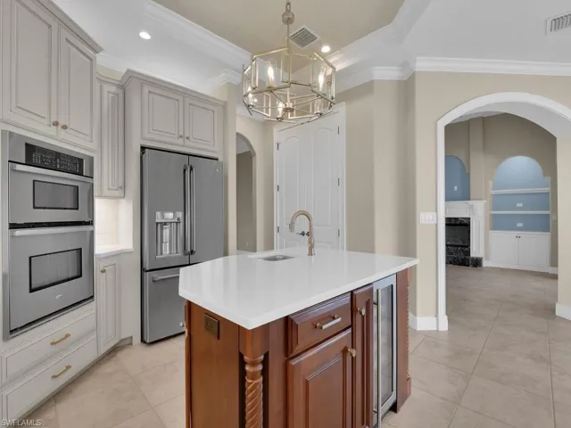 Kitchen featuring sink, crown molding, an island with sink, stainless steel appliances, and beverage cooler