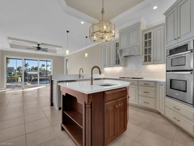 Kitchen with pendant lighting, double oven, an island with sink, sink, and a tray ceiling