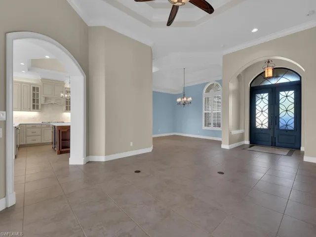 Tiled foyer entrance featuring a raised ceiling, ornamental molding, ceiling fan with notable chandelier, and french doors