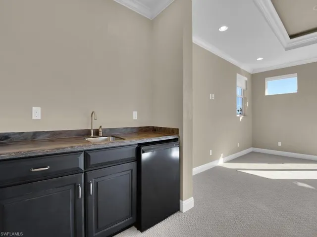 Entertainment room Bar featuring ornamental molding, mini fridge, sink, and light carpet