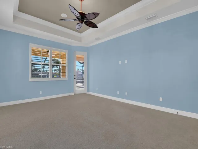 Master bedroom door onto lanai with ceiling fan, ornamental molding, a tray ceiling, and carpet floors