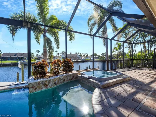 View of pool featuring an in ground hot tub, a water view, a patio area, and glass enclosure