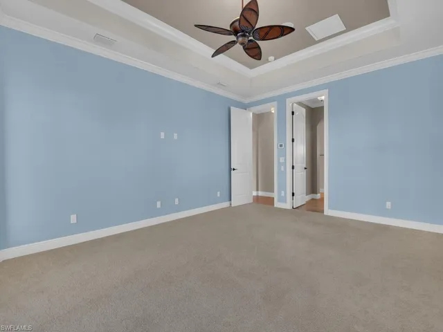 Master bedroom entrance and into bathroom and closets with crown molding, a tray ceiling, carpet floors, and ceiling fan