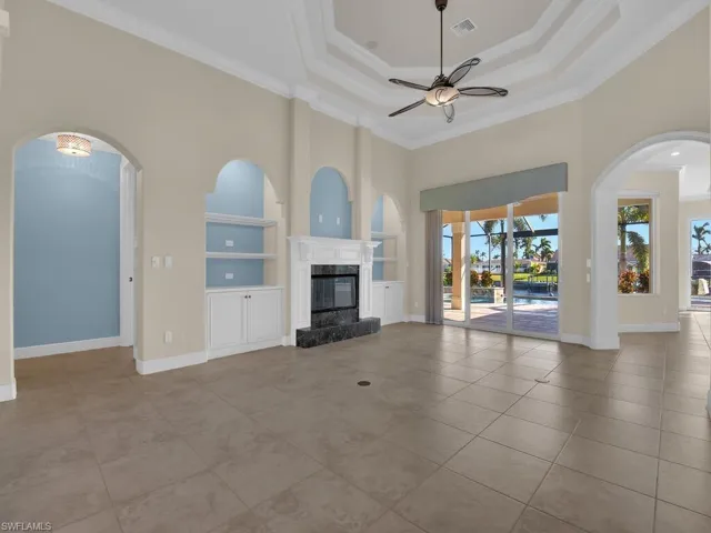 Unfurnished living room featuring ornamental molding, a tray ceiling, built in features, ceiling fan, and a fireplace