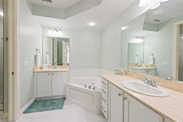 Bathroom with a marble finish shower, two vanities, a bath, and light marble finish flooring