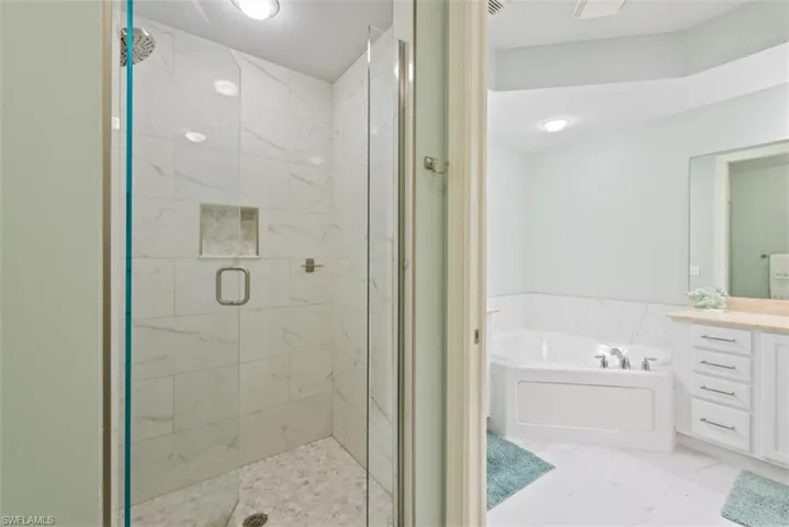 Full bath featuring vanity, a marble finish shower, a bath, and light marble finish floors