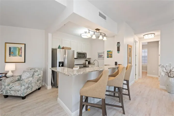 Kitchen featuring appliances with stainless steel finishes, light stone counters, light wood-style floors, a kitchen bar, and white cabinetry