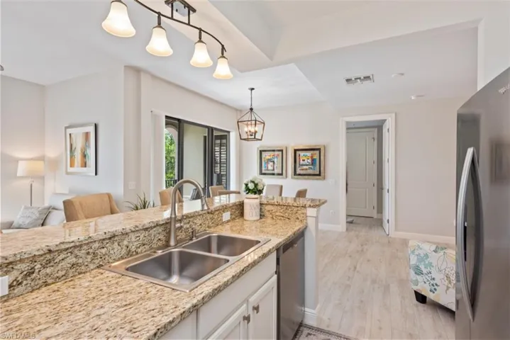 Kitchen with appliances with stainless steel finishes, hanging light fixtures, white cabinets, and light stone counters