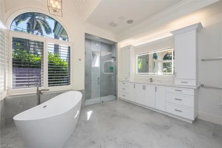Full bathroom featuring a freestanding bath, vanity, a stall shower, light marble finish floors, and ornamental molding