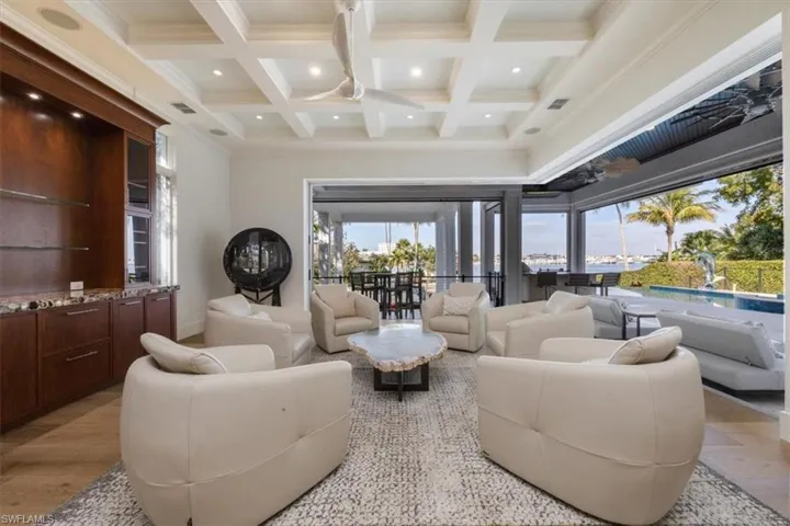 Living room with a high ceiling, light wood finished floors, coffered ceiling, beamed ceiling, and recessed lighting