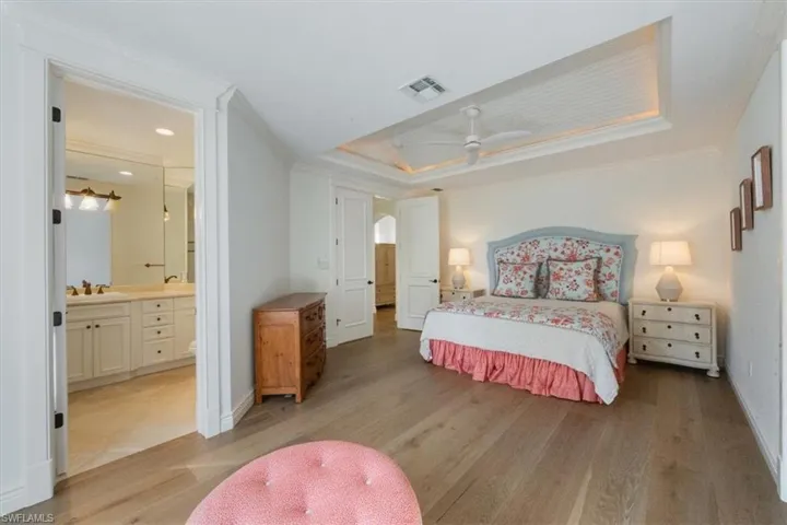 Bedroom featuring light wood-style flooring, ornamental molding, a ceiling fan, a raised ceiling, and ensuite bath