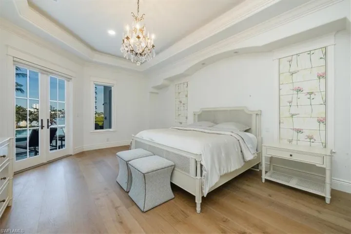 Bedroom featuring access to exterior, light wood finished floors, a tray ceiling, a chandelier, and ornamental molding