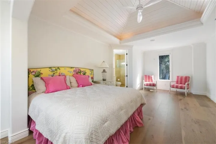 Bedroom featuring wood-type flooring, ornamental molding, connected bathroom, a ceiling fan, and a tray ceiling