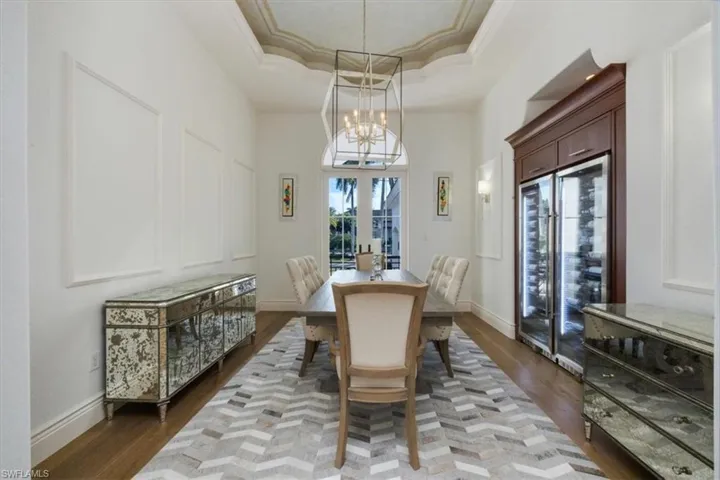 Dining room with beverage cooler, a raised ceiling, crown molding, dark wood-type flooring, and a chandelier