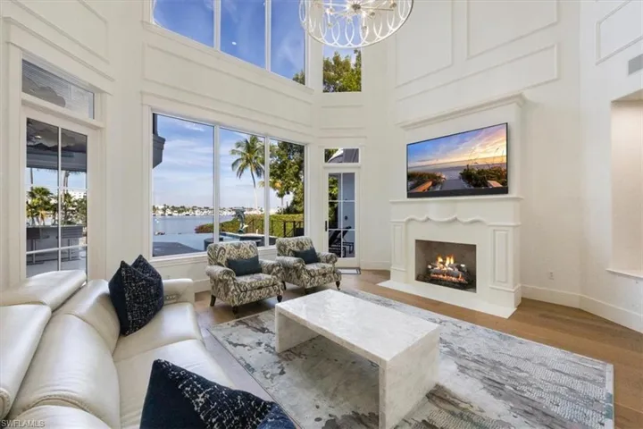 Living area with a fireplace with flush hearth, a towering ceiling, healthy amount of natural light, a chandelier, and wood finished floors