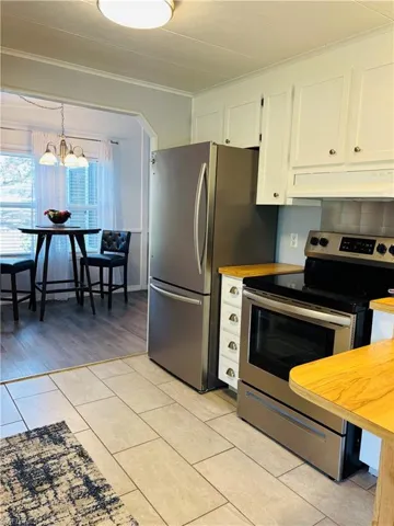 Kitchen with stainless steel appliances, white cabinets, under cabinet range hood, light tile patterned floors, and crown molding