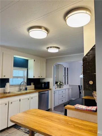 Kitchen with wooden counters, white cabinets, dishwasher, black microwave, and a textured ceiling